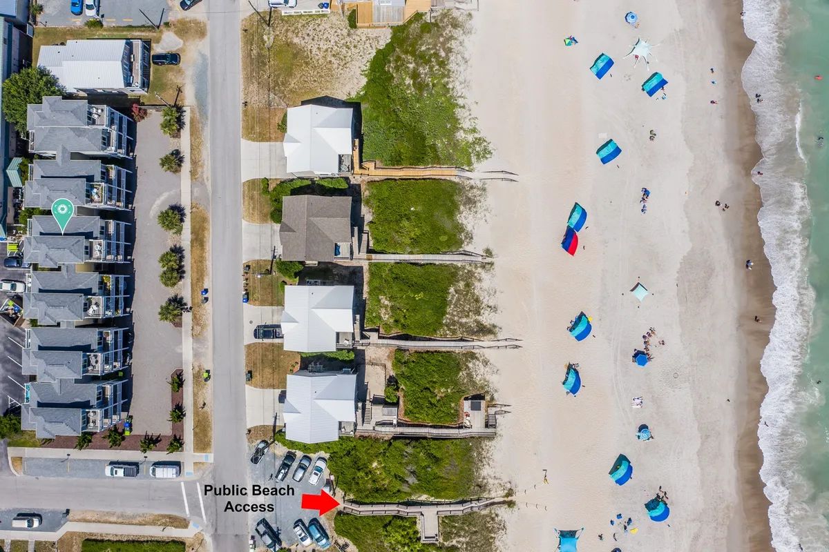 A colorful beach access path leads directly to the water, lined with vibrant umbrellas and groups enjoying beach outings. Cars are parked nearby, highlighting the convenient access. Families are seen picnicking, playing in the sand, and engaging in water sports, with the sunset casting a warm glow over the scene.