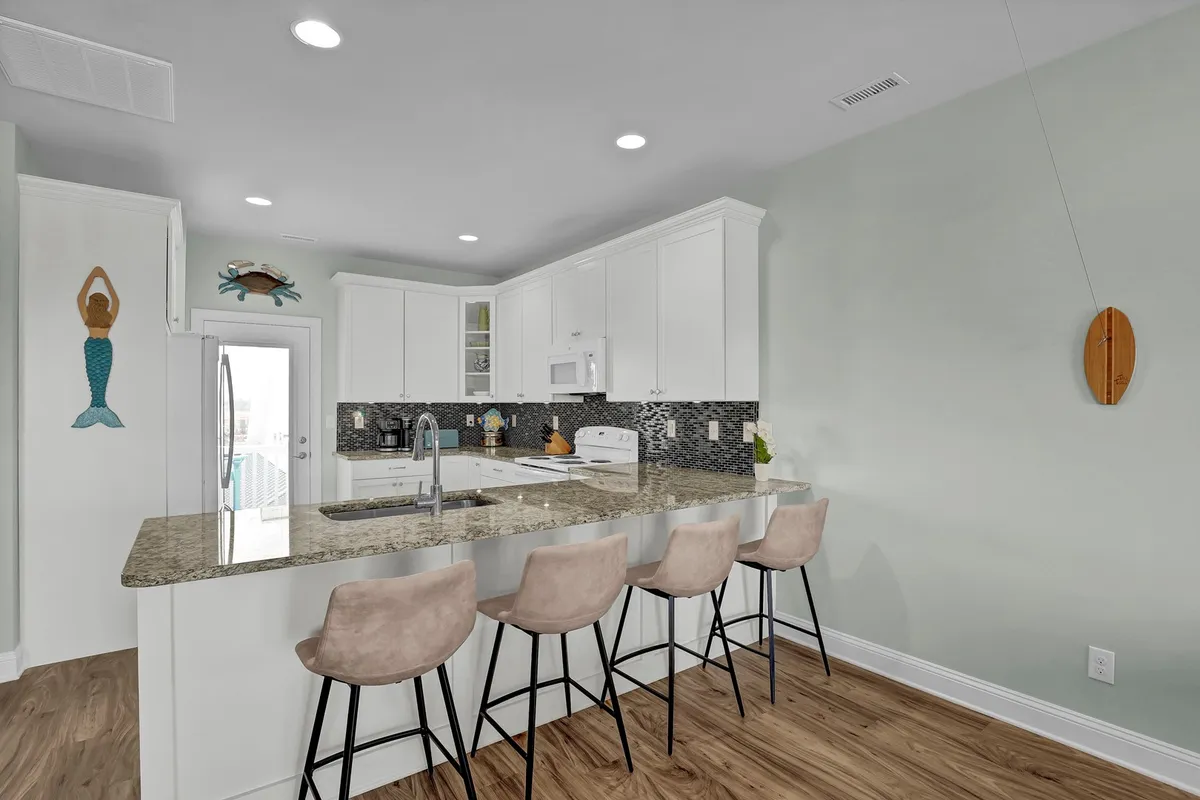 A kitchen scene featuring a central island with bar stools, decorative wall art, and an open, well-lit design. The space is set up to encourage group interaction and easy movement, reinforcing the kitchen's role as a gathering spot.