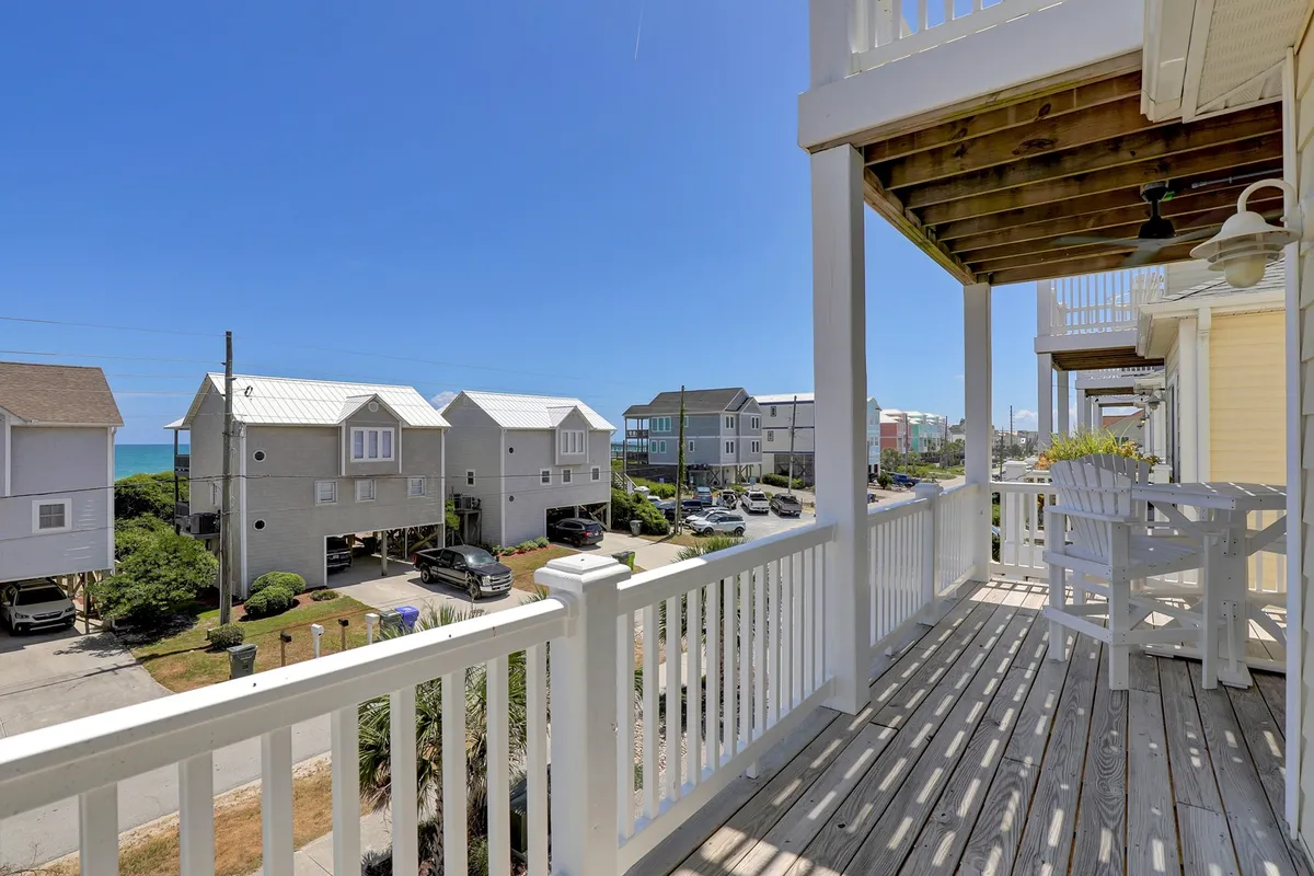 A balcony with a sturdy railing offers a sweeping view of the ocean and neighboring beach homes. Outdoor seating invites residents to linger over morning coffee or evening drinks while soaking up the coastal breeze. The scene captures the inviting atmosphere of the deck, perfectly framing the vibrant, sunlit community beyond.