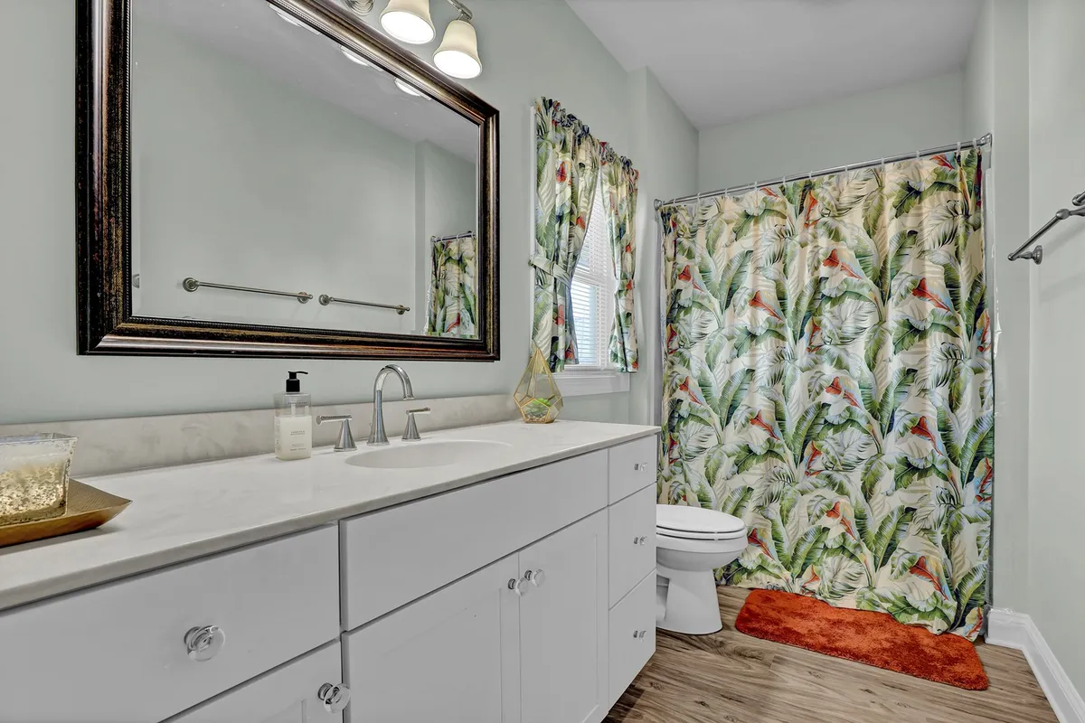 A bright bathroom with a large mirror, a floral shower curtain, and a vanity sink. The mood is refreshing and cheerful, offering a glimpse of the well-appointed bathrooms available to guests.