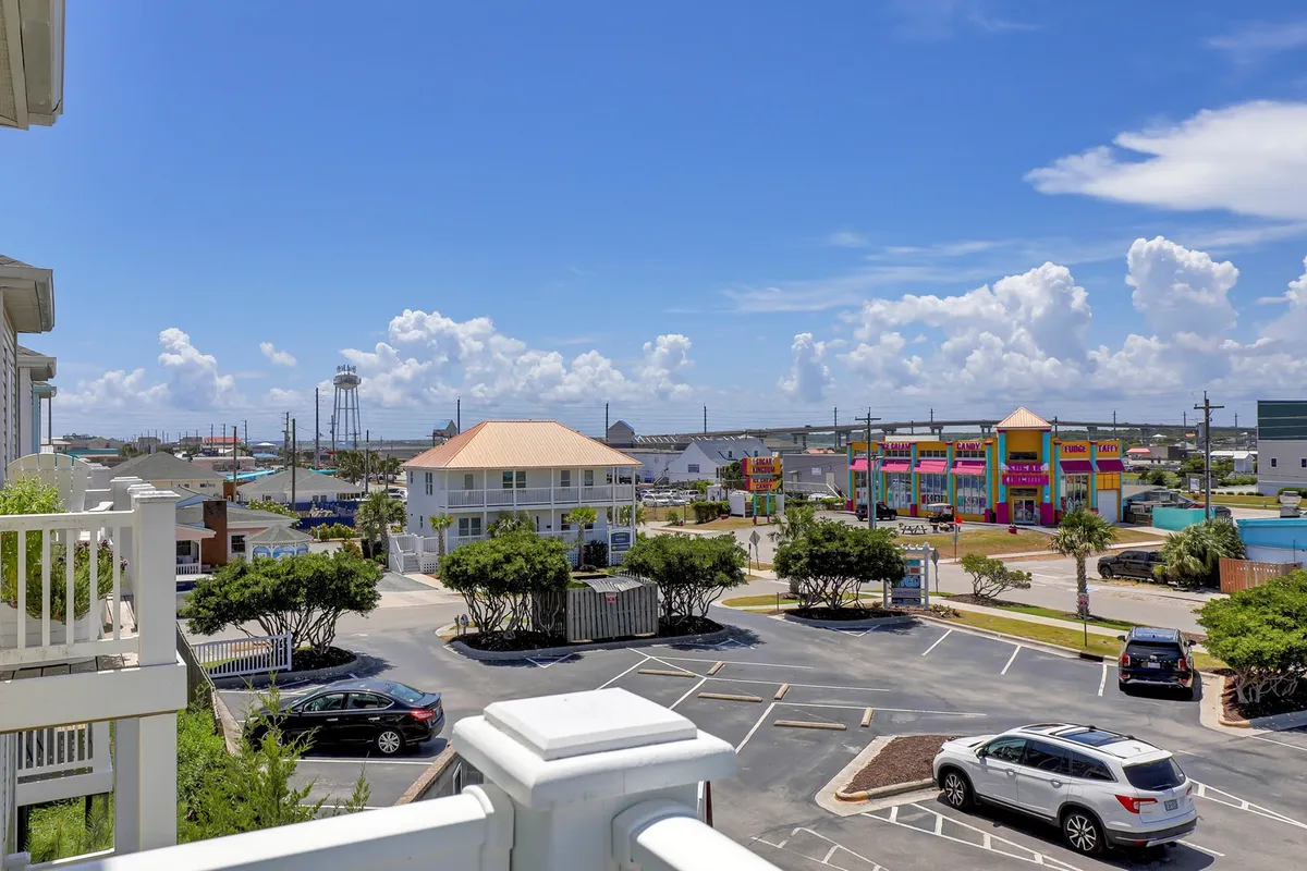 A wide view of the local streetscape featuring colorful buildings, a water tower, and green landscaping. The lively area hints at nearby shops, restaurants, and entertainment options, with parked cars suggesting easy access and a bustling neighborhood vibe.