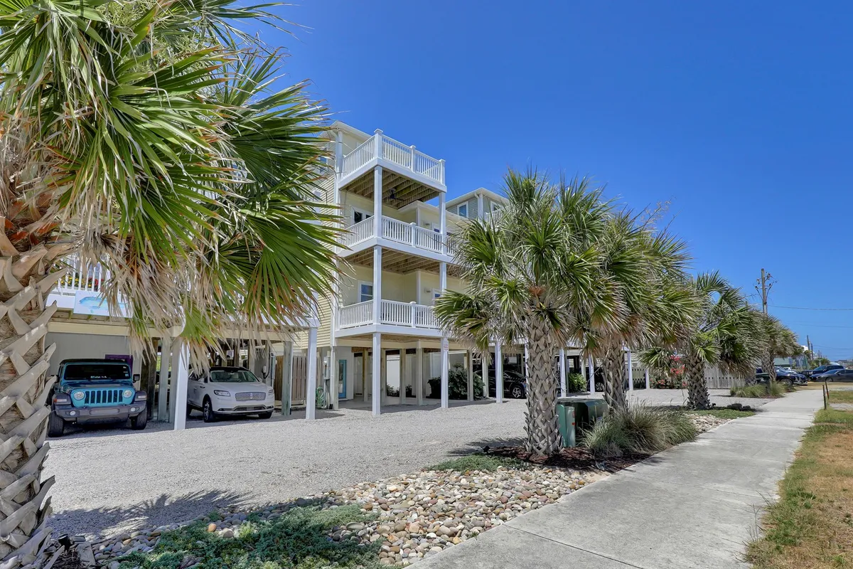 A cheerful exterior scene featuring a multi-level building surrounded by mature palm trees and a well-kept gravel driveway. The setting suggests relaxation outdoors, opportunities for social gatherings, and easy access to nearby attractions. Sunset views are visible from the upper balconies, and there are inviting spots for morning coffee under the palm trees.