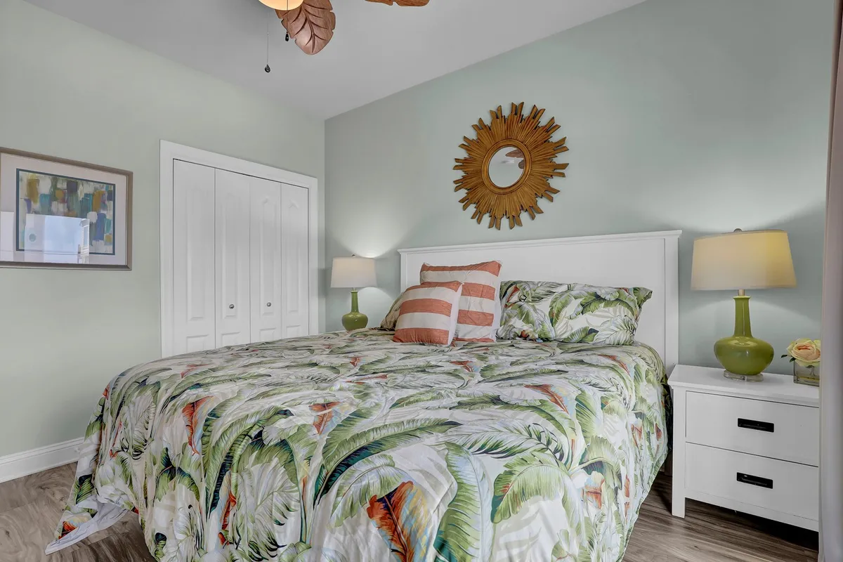 A cheerful bedroom with a bed adorned in tropical-patterned bedding, a sunburst mirror on the wall, striped throw pillows, and bedside table lamps. Natural light streams in, creating a bright and refreshing ambiance.
